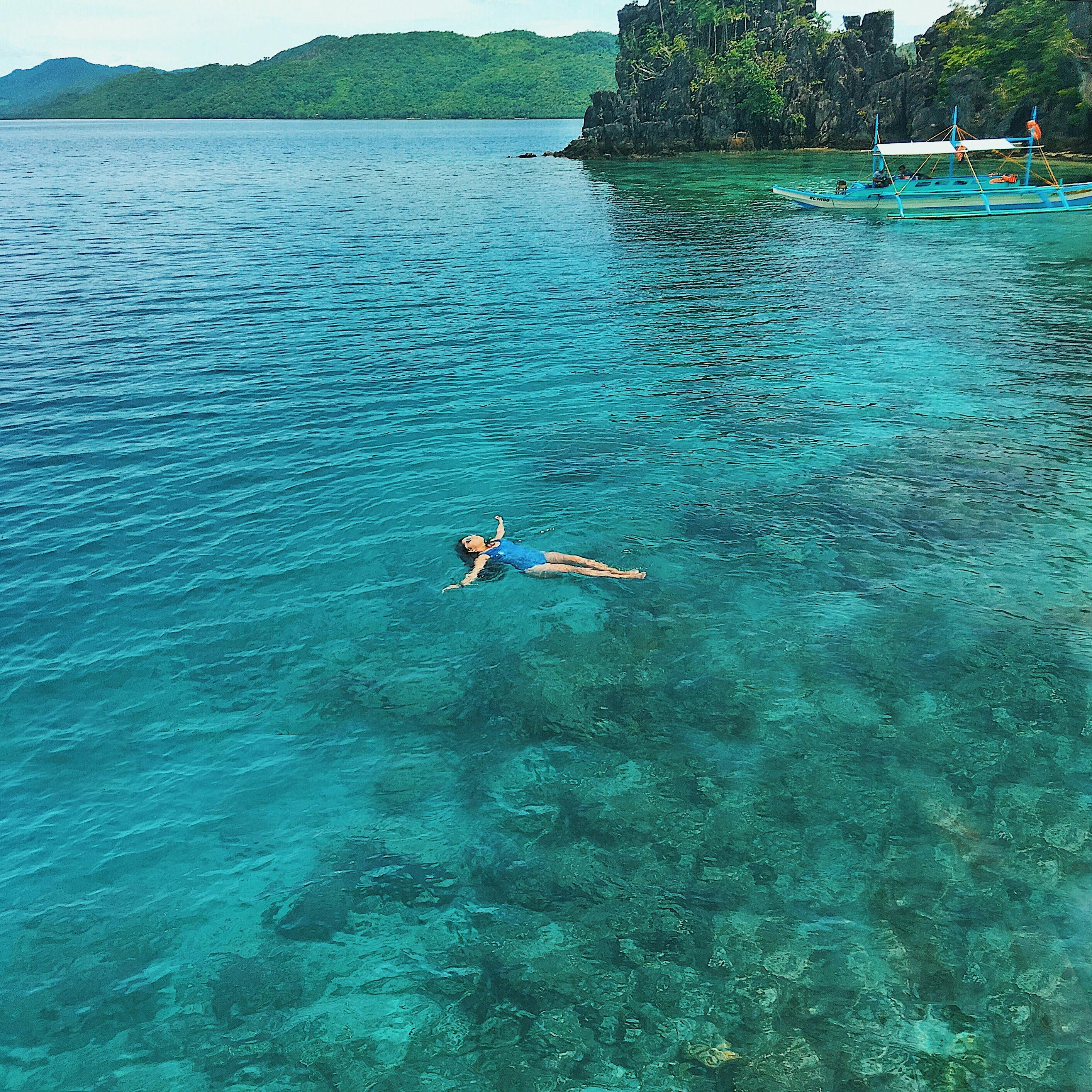 在菲律宾巴拉望，一位妇女漂浮在清澈的绿松石色水面上，四周环绕着茂盛的绿色植物，场面十分放松
