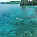 菲律宾巴拉望岛，一名女子漂浮在清澈碧绿的水中，周围环绕着郁郁葱葱的绿色植物