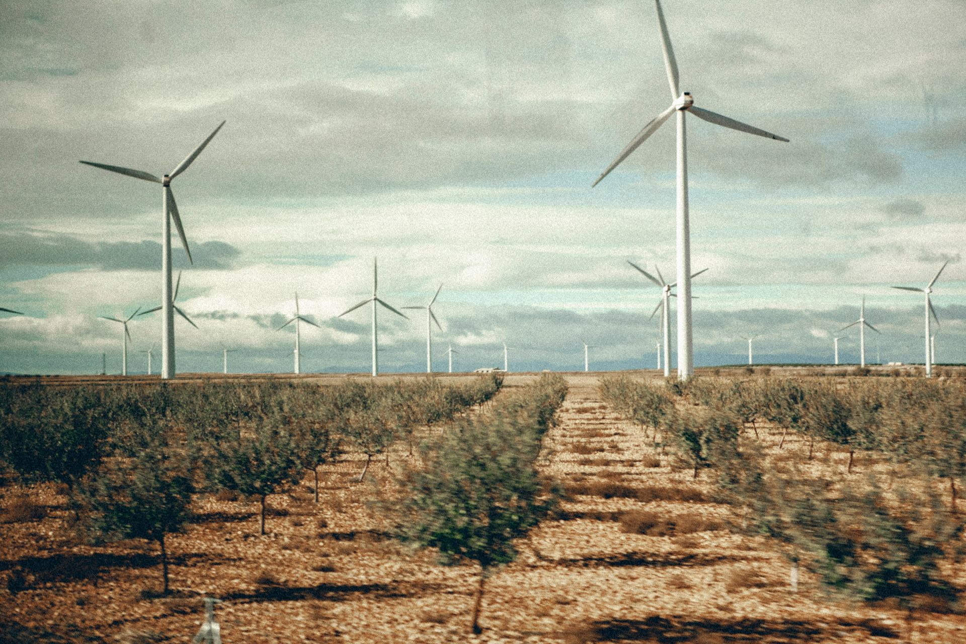 Wind turbines generating renewable energy in a vast rural landscape under a cloudy sky.