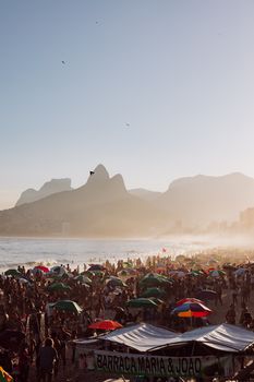 Capture of a lively Ipanema beach with crowds and umbrellas during sunset in Rio de Janeiro.