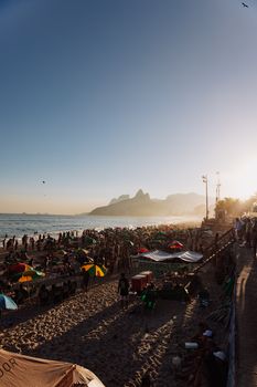 Crowded Ipanema Beach during a vibrant summer sunset in Rio de Janeiro, Brazil.