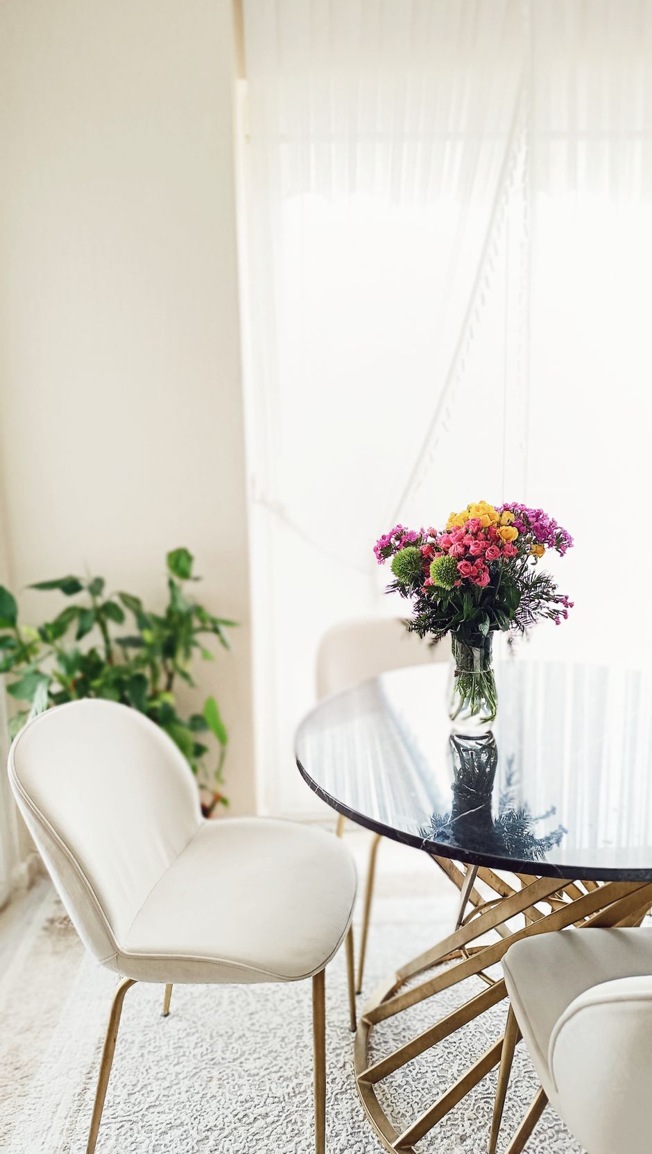 Bright dining area featuring a black table, white chairs, and a colorful flower bouquet centerpiece.