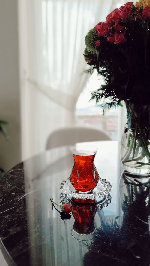 Free A glass of tea on a marble table beside a vibrant floral arrangement in a vase. Stock Photo