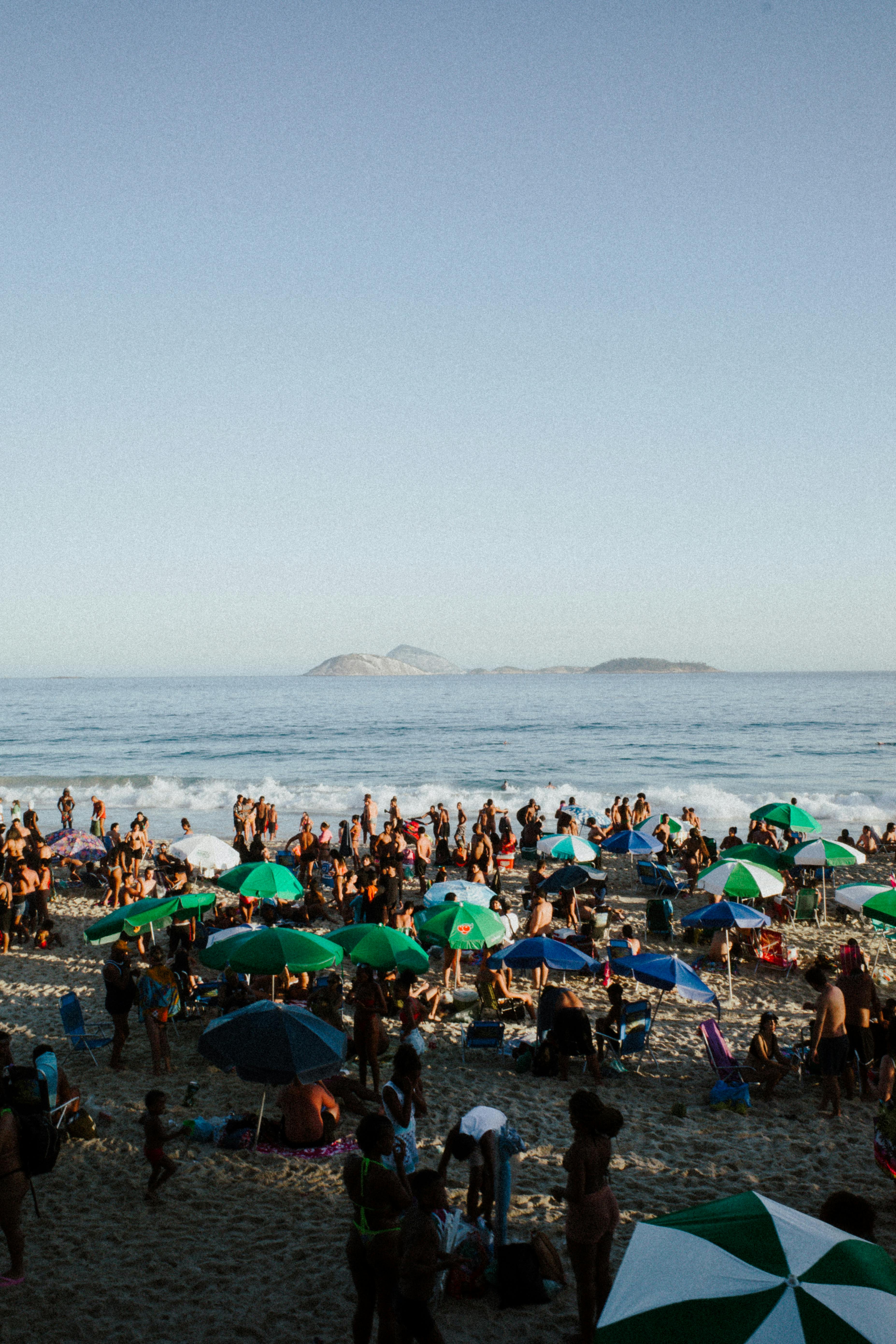 A lively beach scene in Rio de Janeiro with a crowd, umbrellas, and ocean view.