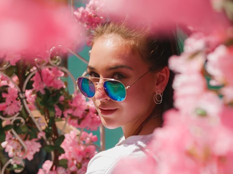 阳光明媚的日子里，一个开朗的女人戴着墨镜，站在充满活力的粉红色花丛中