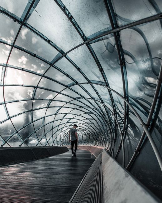 A man walking through a modern and futuristic glass tunnel in an urban setting.