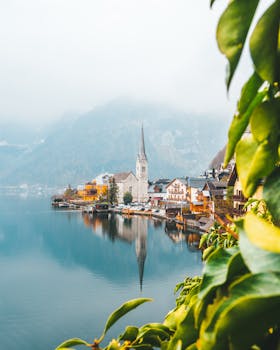 秋天，湖滨村庄宁静迷人，云雾缭绕的山脉与生机勃勃的树叶相映成趣