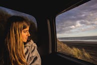 一名年轻女子从车窗向外凝视，欣赏白天美丽的海滩景色