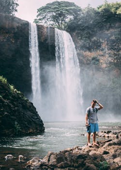 一名男子站在靠近大瀑布的岩石上，四周环境郁郁葱葱，充满自然气息