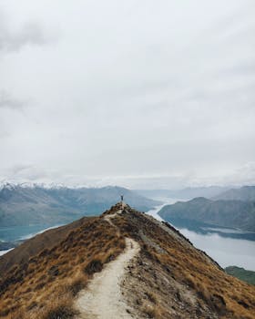 A lone hiker enjoys a breathtaking mountain view, surrounded by nature and tranquil skies.