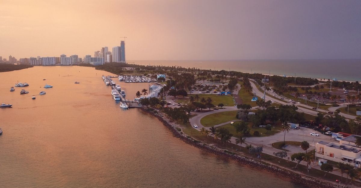 A stunning aerial view of a coastal cityscape with modern architecture and a serene harbor at sunset.
