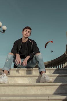 在晴朗的天空下，时尚的年轻人站在大理石台阶上摆姿势，背景是滑翔伞