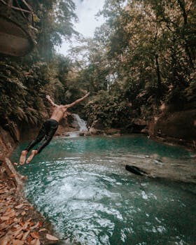 在菲律宾安特克拉，一名男子跳入一个碧绿的天然水池，周围环绕着郁郁葱葱的森林