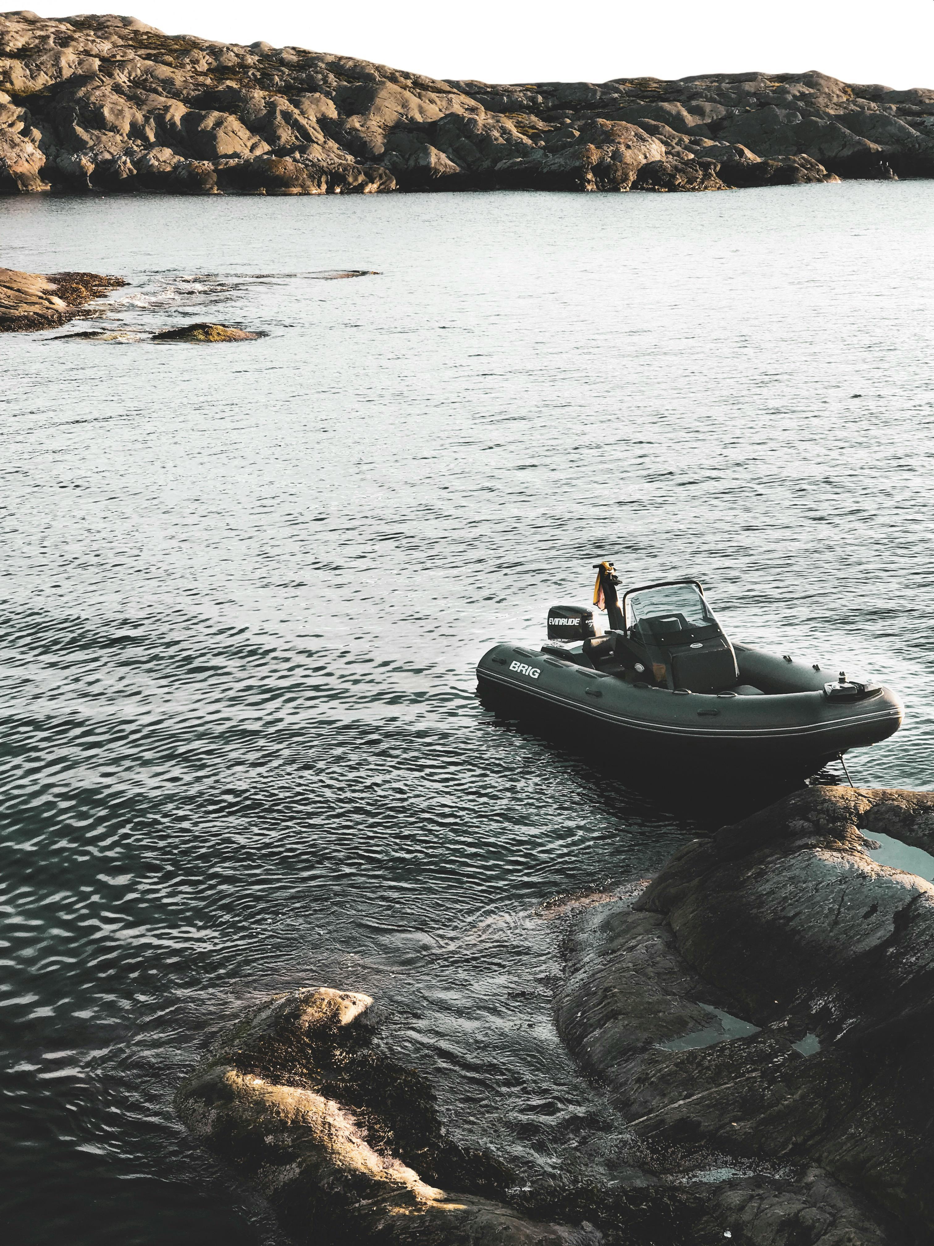 Motorboat anchored near rocky shore in a calm sea setting with rugged coastal landscape.