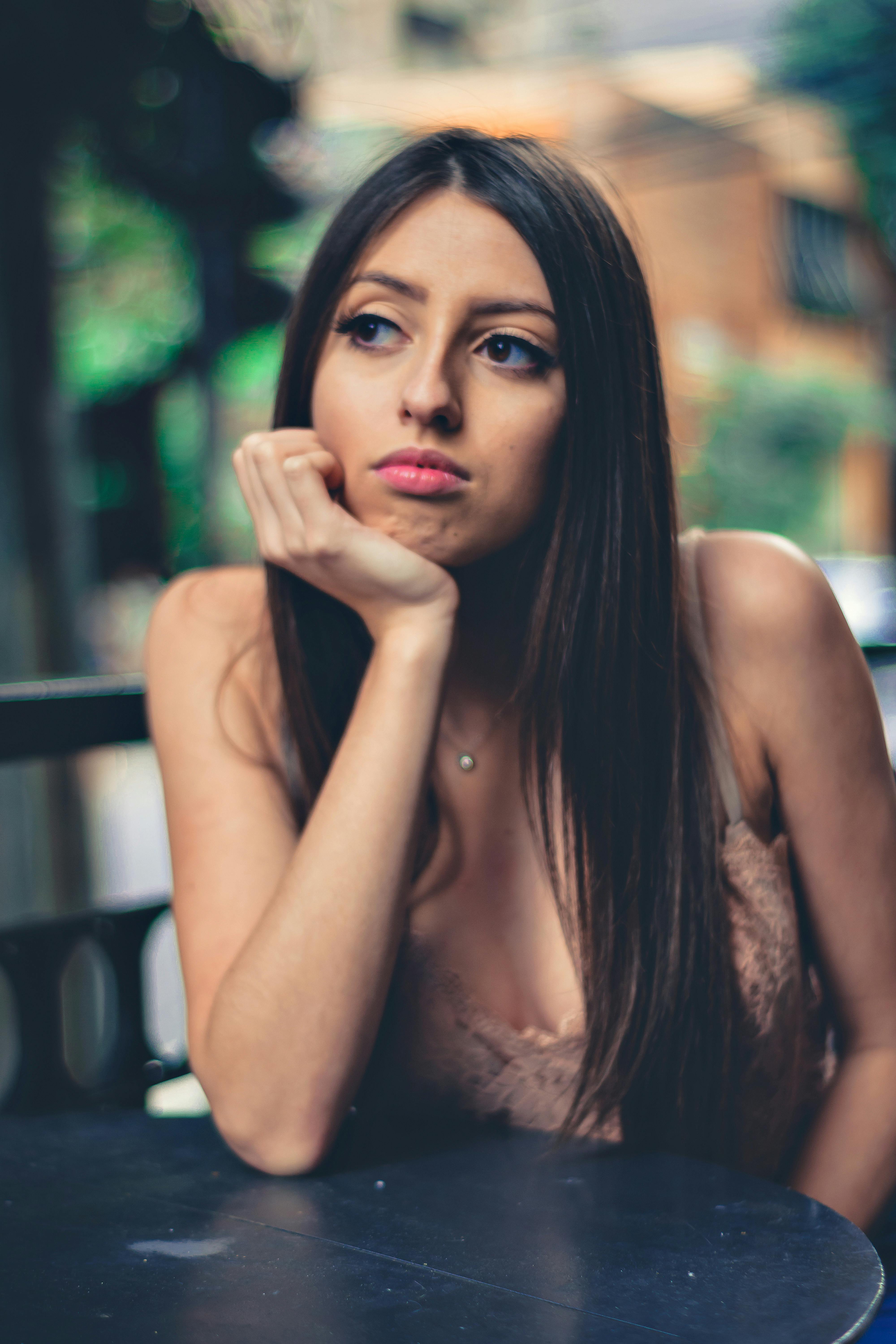一位黑发女子穿着休闲装，沉思地坐在户外桌旁
