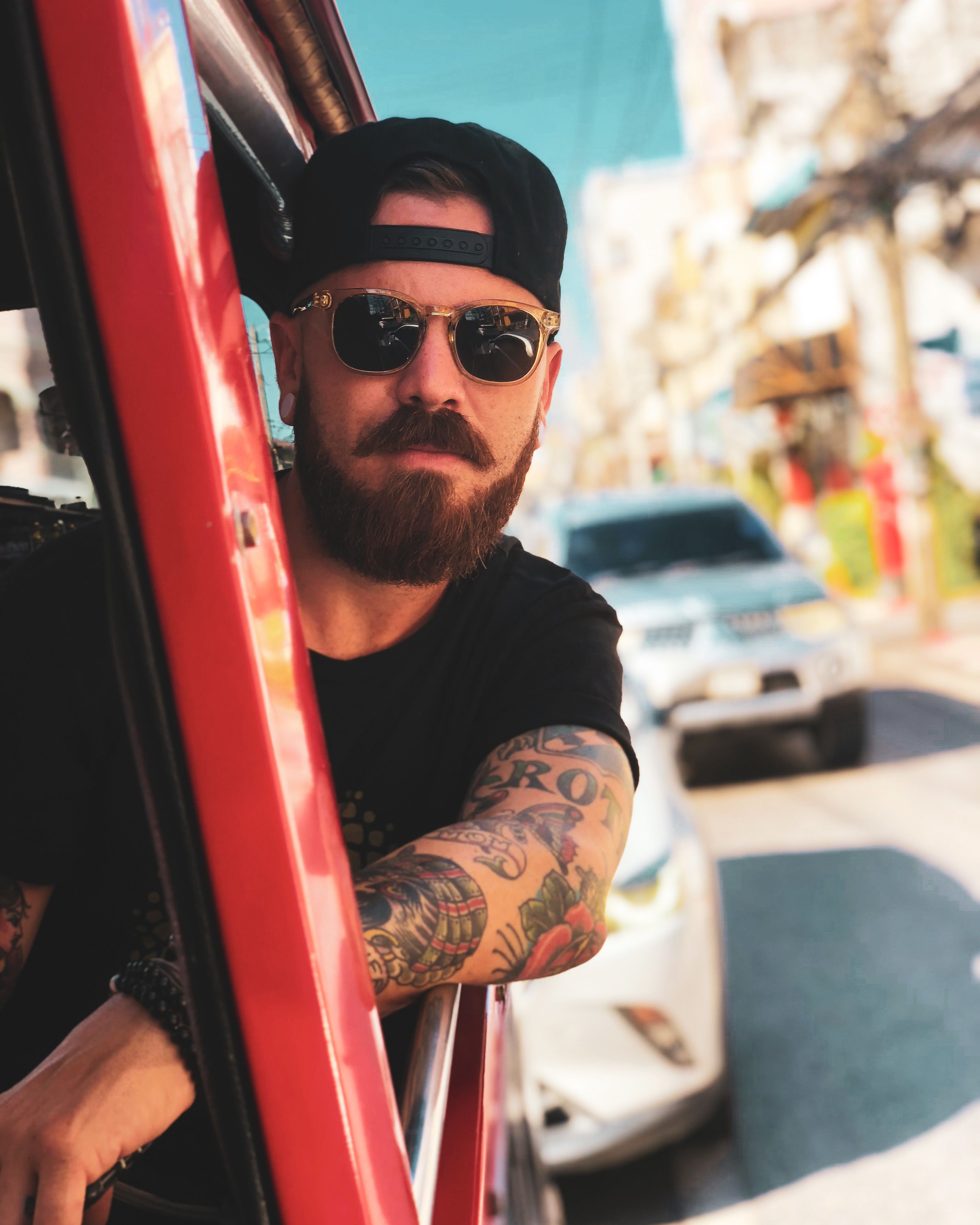 Man with tattoos and sunglasses enjoying a ride in vibrant Phuket street.