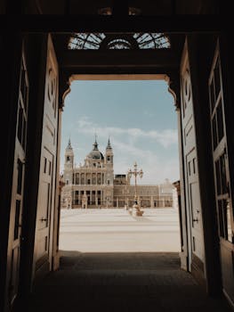 A stunning view of Madrid's Almudena Cathedral framed by an ornate doorway from the Royal Palace.