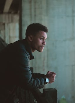 一个穿着休闲装的年轻男子靠在金属栏杆上，看起来若有所思