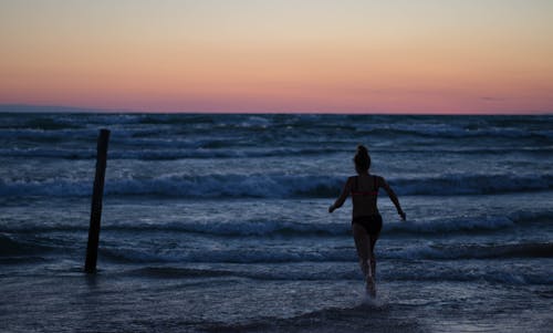Free Woman Running Towards Body of Water Stock Photo