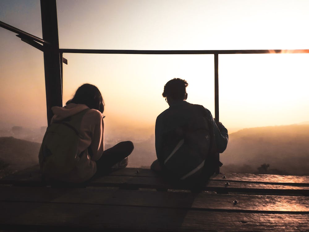 Two Persons Sitting by the Deck Facing Sunrise