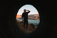 日落时分，一名戴着棒球帽的男子在隧道中欣赏风景优美的沿海景观