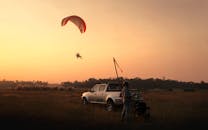日落时分，空地上，一架滑翔伞和一辆皮卡车的剪影捕捉到了一个冒险时刻