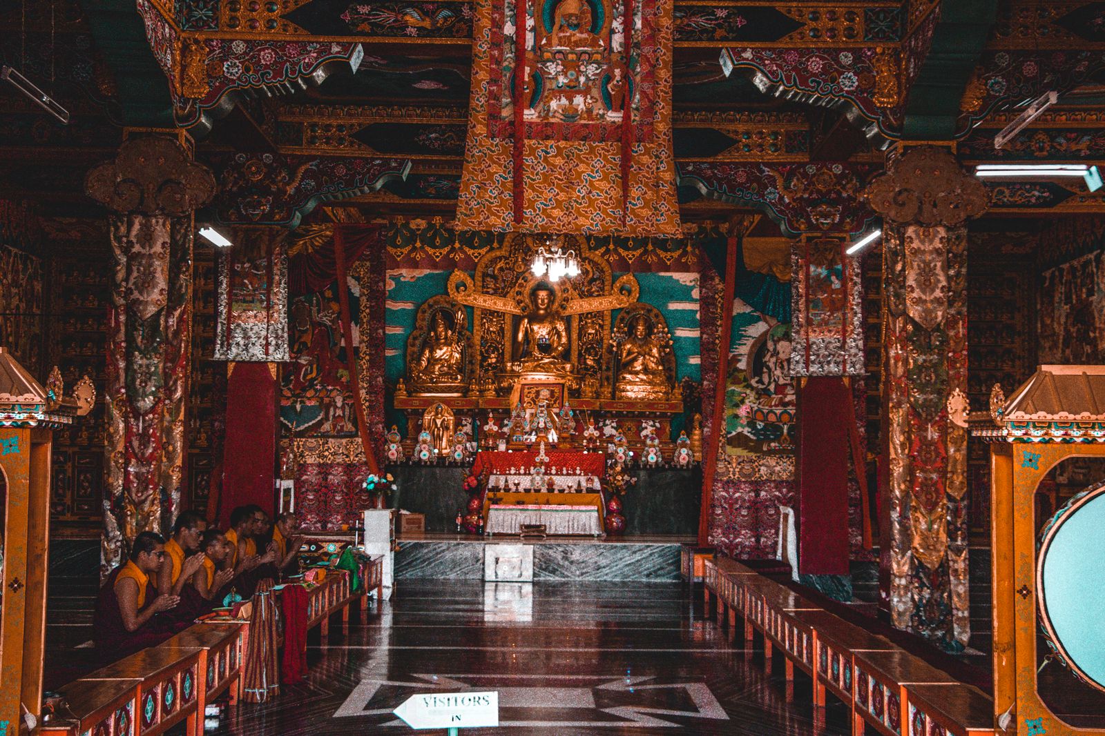 Young monks at prayer in the painted assembly hall of a Gangtok monastery, golden Buddhas on the altar beyond