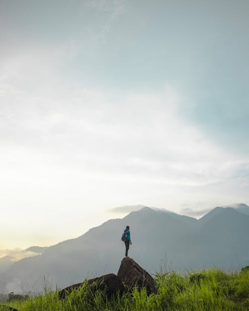Free Person Standing on Brown Rock Formation Facing on Mountain Range Stock Photo
