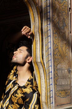 一名男子闭着眼睛，靠在华丽的墙壁上摆姿势，在阳光下展现时尚与休闲