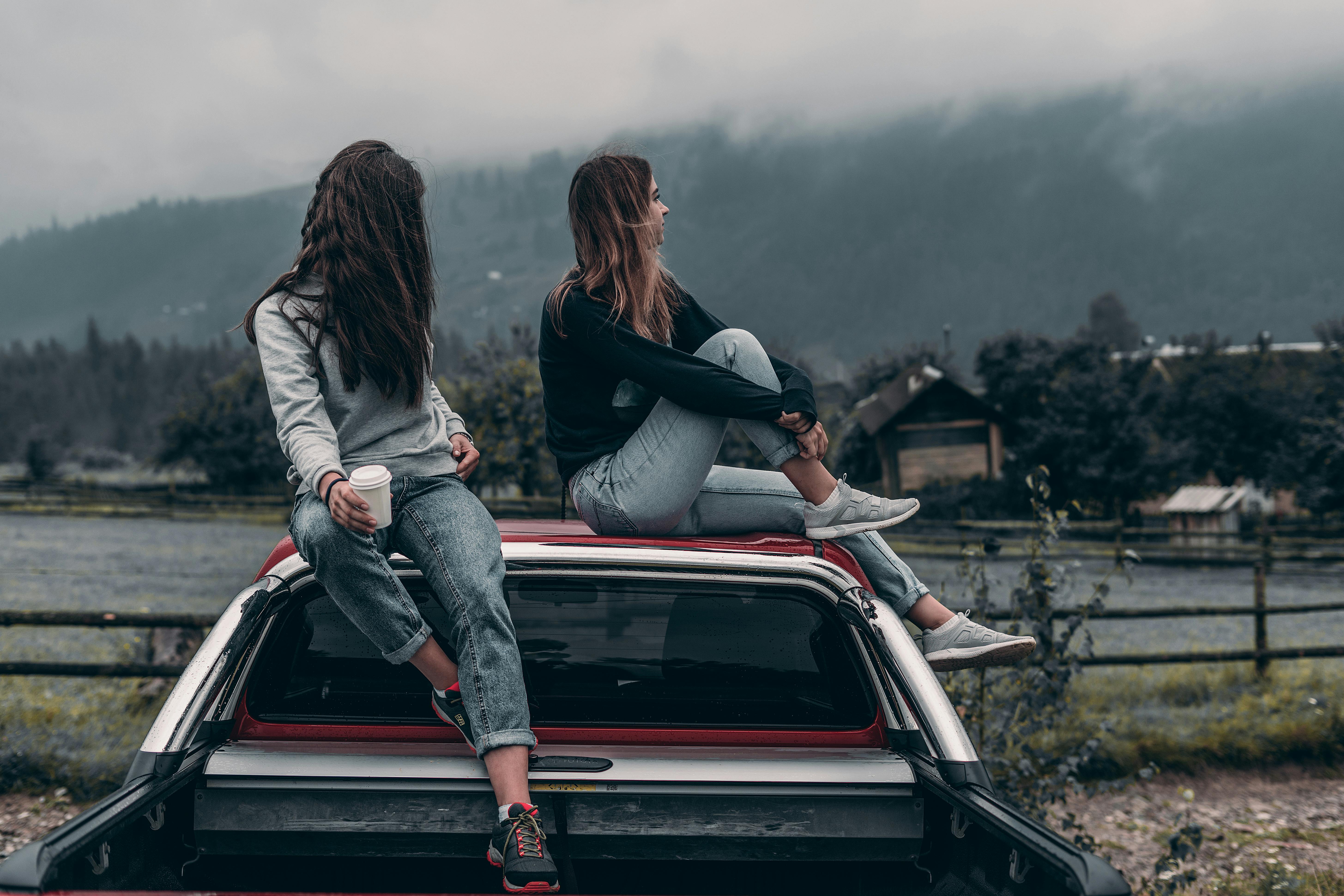 Two women sitting on a vehicle roof. | Photo: Pexels