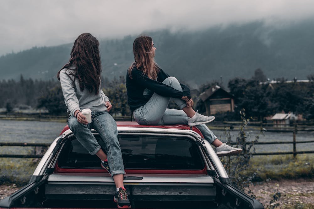 Two women sitting on the vehicle roof. | Photo: Pexels
