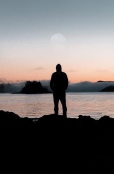 平静的水域上，一个孤独的人在日落余晖中勾勒出轮廓