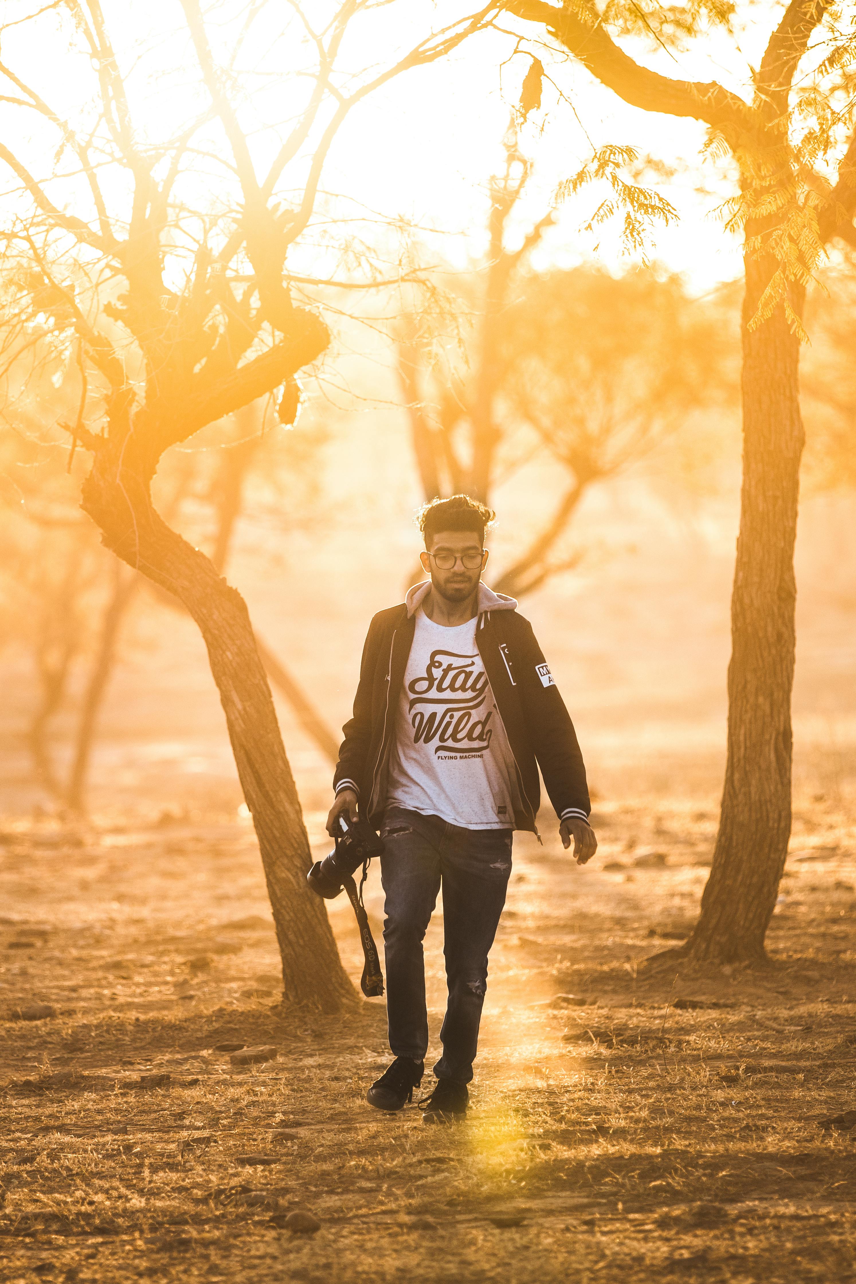 Man with a camera walks through a sunlit forest, capturing the golden glow of dusk.