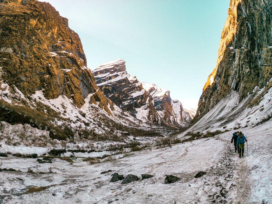 Hikers trekking through a snow-covered mountainous landscape on a bright day.
