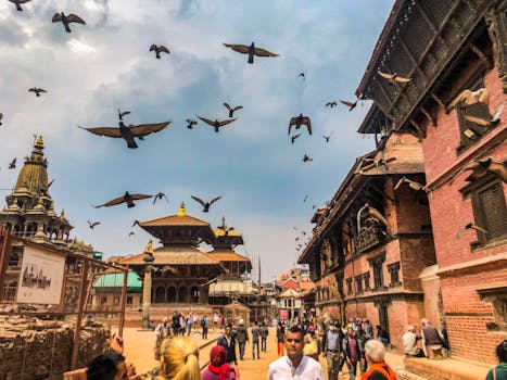 Vibrant scene at Patan Durbar Square with people, pigeons, and traditional Newari architecture under a cloudy sky.