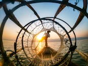 日落时分，渔民在宁静的湖面上保持平衡，撒网捕鱼，天空充满活力