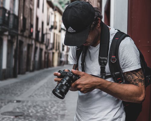 Photo of Man Standing in Alley Holding Dslr Camera Looking at Photos