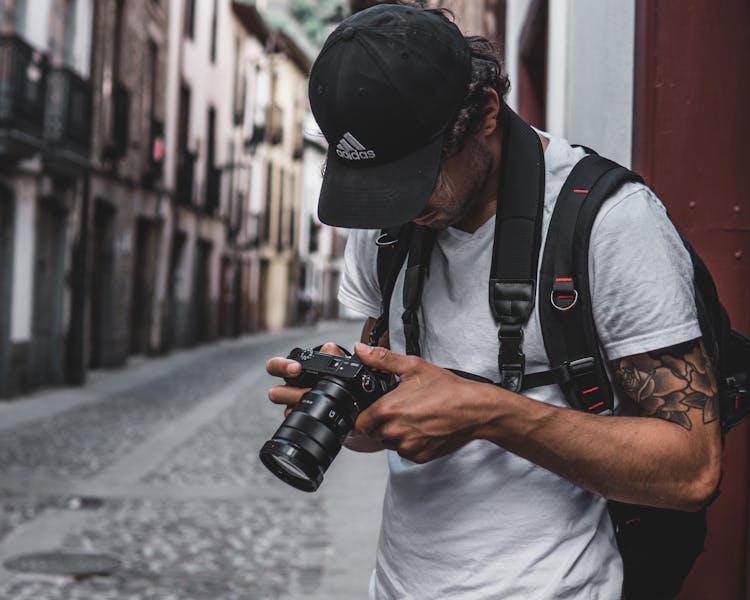 Photo Of Man Standing In Alley Holding Dslr Camera Looking At Photos