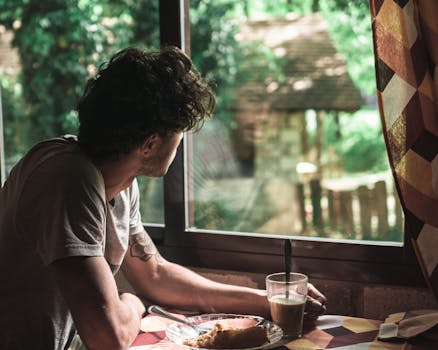 Man enjoying morning coffee indoors, looking outside through a window.