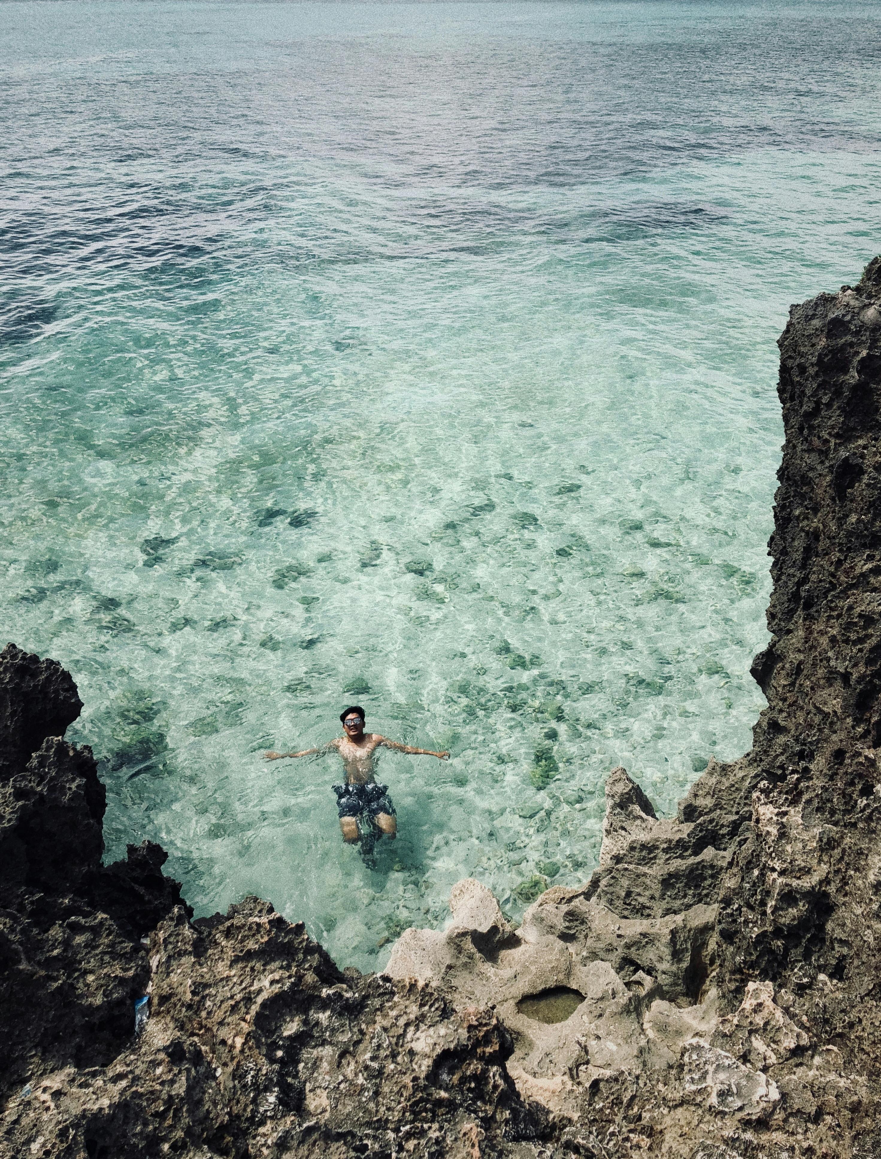 一名男子喜欢在清澈碧绿的海水中游泳，周围环绕着岩石悬崖