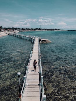 一个孤独的人走在延伸到清澈蔚蓝大海的木制码头上，可以欣赏到美丽的海滨景色