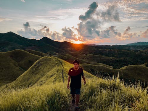 Free Man Walking in Ridge of Grass Covered Hill at Sunset Stock Photo