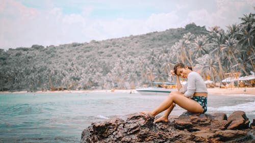 Photo of Smiling Woman Sitting on Rocks Near Beach