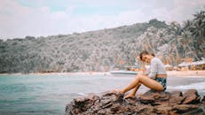 一个女人坐在海边的岩石上，享受着热带海滩上阳光明媚的一天