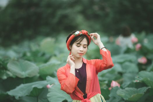一位身着明艳红裙的娴静女子，在郁郁葱葱的莲田间优雅地摆着姿势