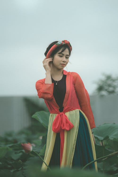 Selective Focus Photo of Woman in Colorful Outfit Posing with Her Eyes Closed Standing in the Middle of Flower Field