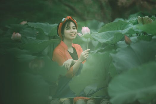 亚洲女人在荷花田里热情地微笑着，手里拿着一朵粉红色的莲花