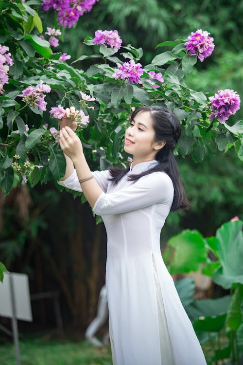 Side View Photo of Smiling Woman in White Dress Picking Purple-petaled Flowers