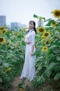 一位穿着白色连衣裙的女士站在盛开的向日葵之中，沉思着