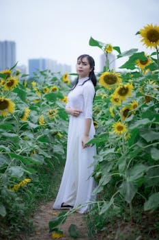 一位穿着白色连衣裙的女士站在盛开的向日葵之中，沉思着